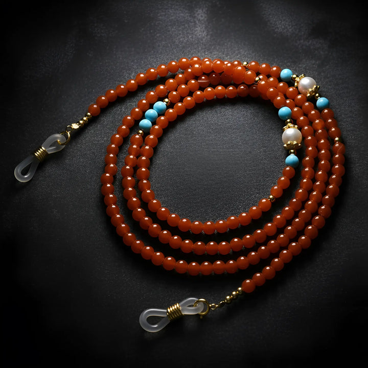 Red agate eyeglass chain displayed on velvet background, highlighting warm gemstone tones and elegant handmade details by Oculux Jewelry.